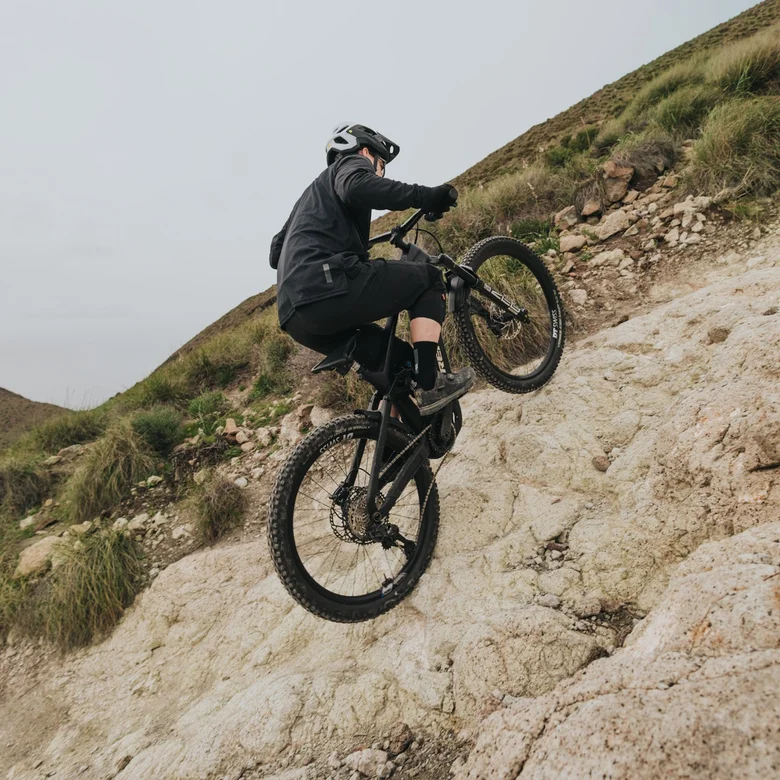 An eMountain biker climbs an extremely steep and rocky slope, shifting his weight forward to master the demanding climbing.
