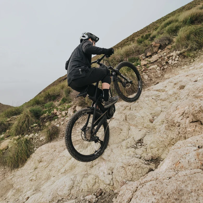 Een eMountainbiker klimt een extreem steile en rotsachtige helling op. Hij verplaatst zijn gewicht naar voren om de veeleisende stijging te beheersen.