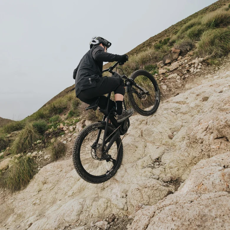 En eMountainbiker klättrar uppför en extremt brant och stenig sluttning. Han flyttar vikten framåt för att bemästra den krävande lutning.
