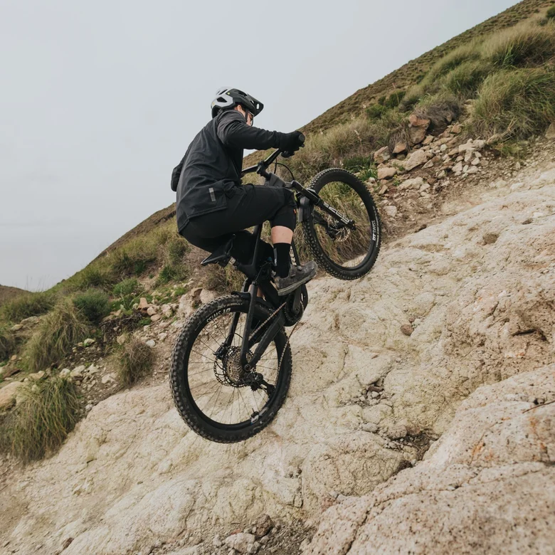 En eMountainbiker klatrer op ad en ekstremt stejl og klippefyldt skråning. Han flytter vægten fremad for at mestre den krævende stigninger.