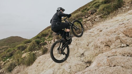An eMountain biker climbs an extremely steep and rocky slope, shifting his weight forward to master the demanding climbing.