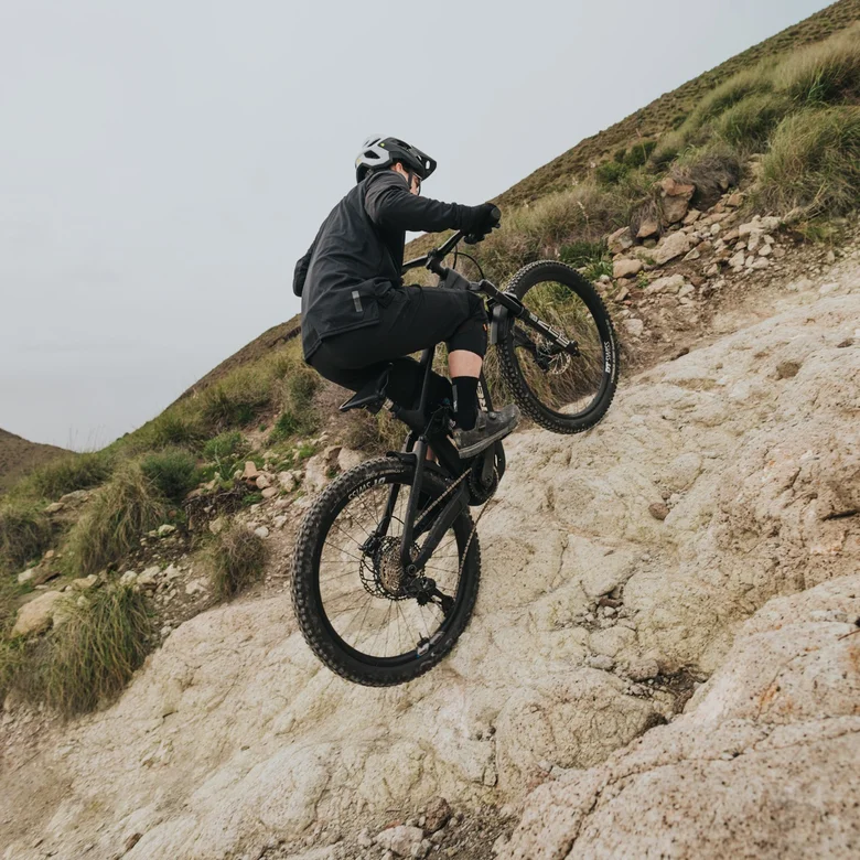 An eMountain biker climbs an extremely steep and rocky slope, shifting his weight forward to master the demanding climbing.