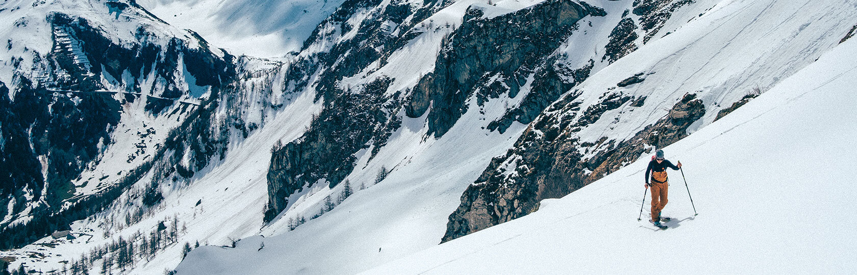 Une femme pratiquant le ski de randonnée, avec des montagnes enneigées en arrière-plan.