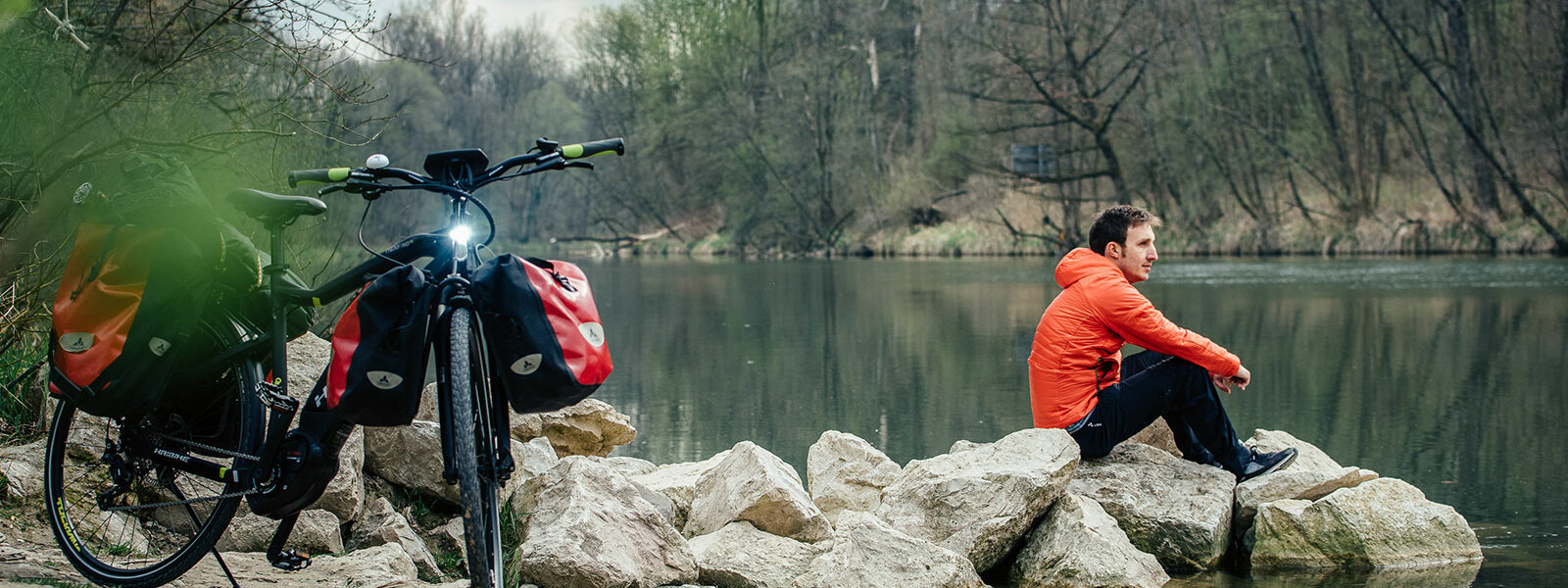 Ein eBiker sitzt an einem See, hinter ihm steht sein Trekking Pedelc mit Gepäcktaschen