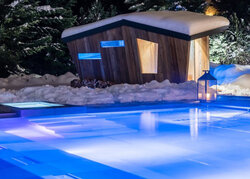 Una vasca idromassaggio all'aperto in inverno, con una sauna in legno sullo sfondo.