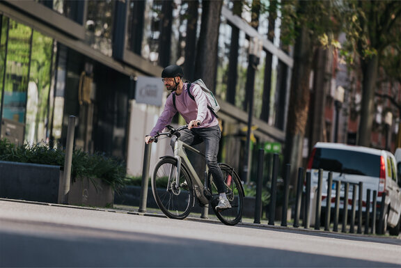 Mann mit Brille und Rucksack fährt auf einem eGravel Bike und biegt auf einer Straße nach rechts ab.