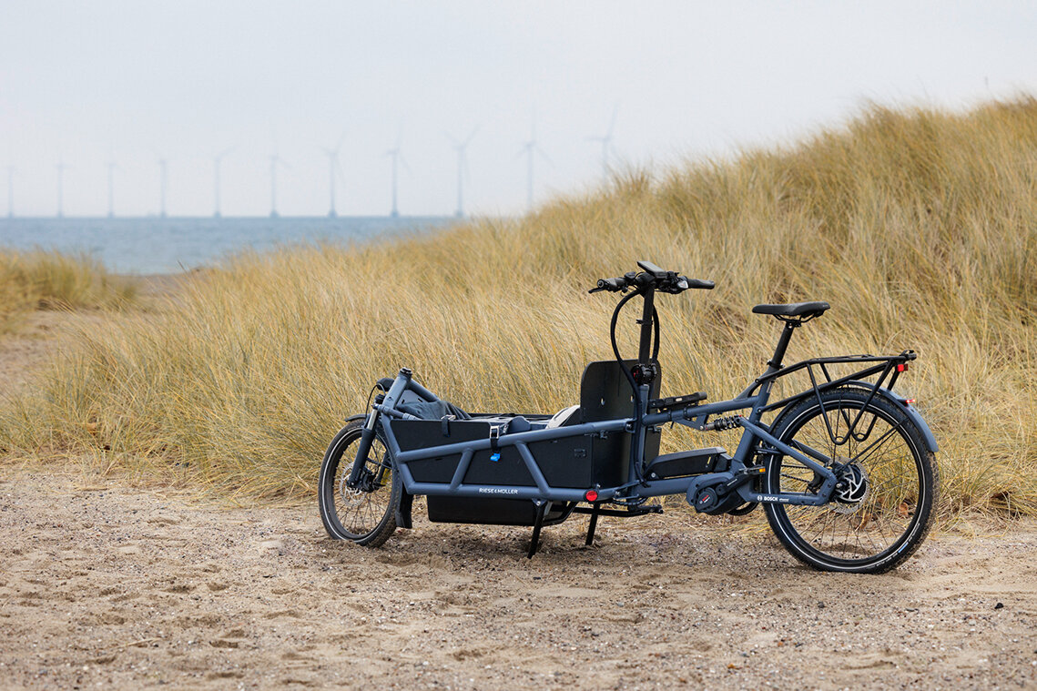 eCargo is standing in front of grass on the beach, with wind turbines visible in the distance.