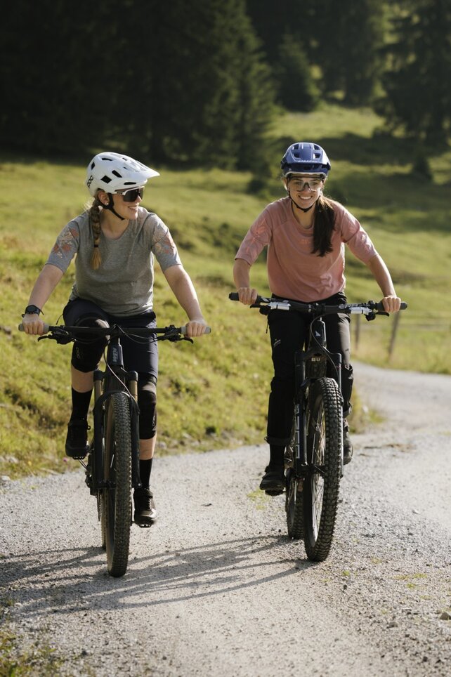 Two eBiker ride one behind the other on a forest path.
