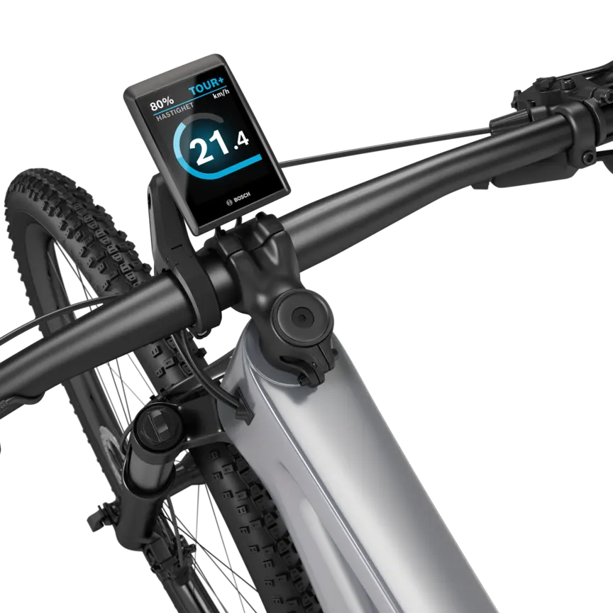 En silverfärgad eMountainbike med svart styre mot en vit bakgrund. En Kiox 500 är monterad på styret. Displayen visar hastigheten i km/h, batteristatus och körläge.