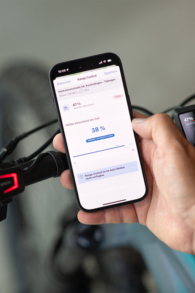 Nahaufnahme eines Smartphones, das vor einem eBike Lenker gehalten wird. Auf dem Screen ist die eBike Flow App zu sehen, in der der Zielakkustand definiert wird.