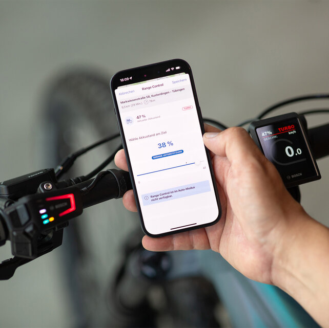 Nahaufnahme eines Smartphones, das vor einem eBike Lenker gehalten wird. Auf dem Screen ist die eBike Flow App zu sehen, in der der Zielakkustand definiert wird.