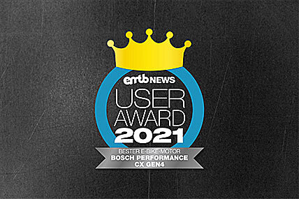 Icon with the text "eMTB NEWS USER AWARD 2021": A golden crown above the text, enclosed by a blue circle. Below it states "BEST E-BIKE MOTOR BOSCH PERFORMANCE CX GEN4". The background has a gray concrete texture.