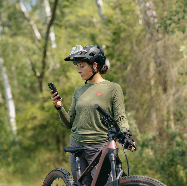 Une femme se tient à côté de son VTT AE et consulte son smartphone.