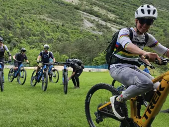 Some eBiker stand with their eBikes on a green field, with a bush-covered hill in the background.