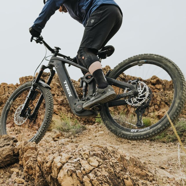 Nahaufnahme eines schwarzen Trek eMountainbikes, das von einem Fahrer über einen schroffen, felsigen Trail manövriert wird. Der Fokus liegt auf dem eBike und dem unwegsamen, steinigen Untergrund, der die technischen Fähigkeiten von Fahrer und Material verdeutlicht.
