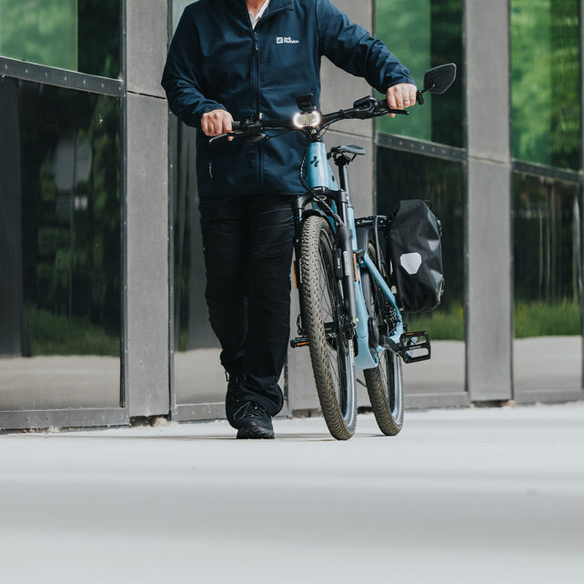 A man wearing a helmet pushes his blue eSUV along a building.