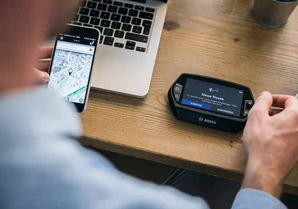 A person sits at a table with a laptop and uploads a new route to the Nyon display via the eBike Flow app.