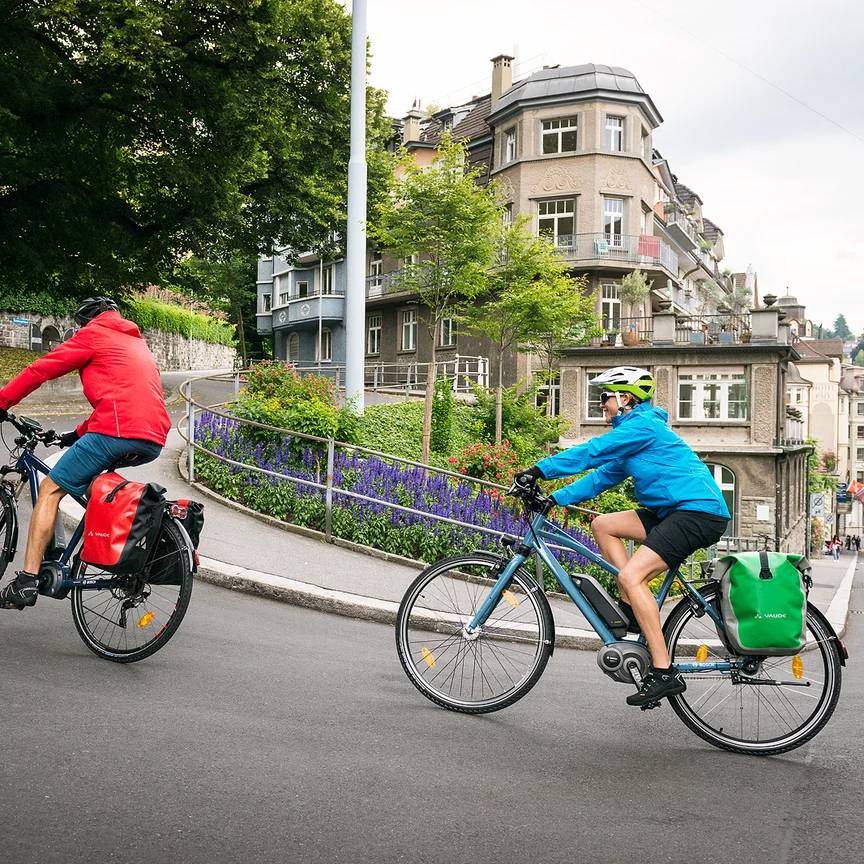Dwaj rowerzyści na e-rowerach pokonują stromą ulicę w mieście.