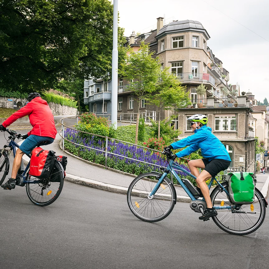 Deux cyclistes sur des vélos à assistance électrique gravissent une rue escarpée en ville.