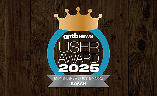 Icon with the text "emtb NEWS USER AWARD 2025": A golden crown above the font, surrounded by a blue circle. At the bottom it says "Most recommended Marke". The background is made of dark wood.