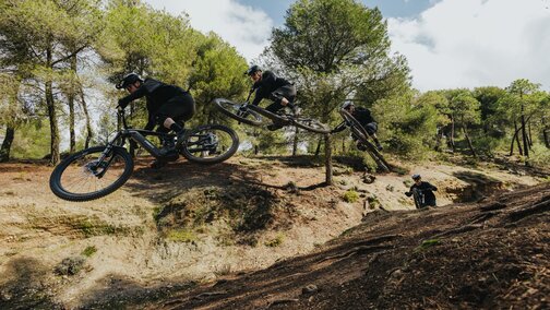 Sequenza di un eMountain biker che esegue un salto su un trail polveroso nel bosco. L'inquadratura mostra il pilota nelle tre diverse fasi del salto: dallo stacco, alla fase di volo, fino all'atterraggio.