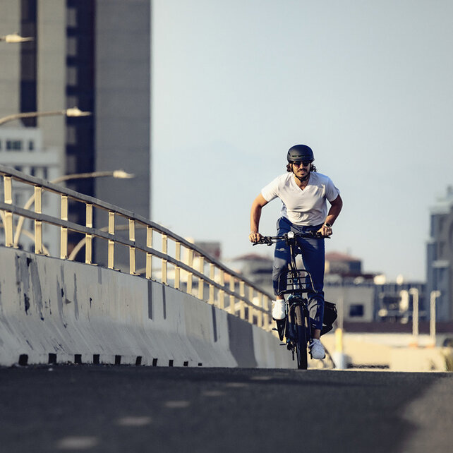 An eBiker rides across a bridge with a city in the background.