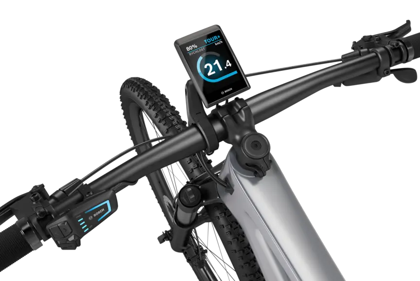 Stříbrné eMountainbike s černým řídítkem na bílém pozadí. Na řídítku je namontován Kiox 500. Displej zobrazuje rychlost v km/h, stav akumulátoru a jízdní režim.