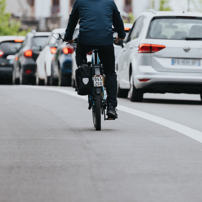 eBiker drives toward a row of stationary cars.