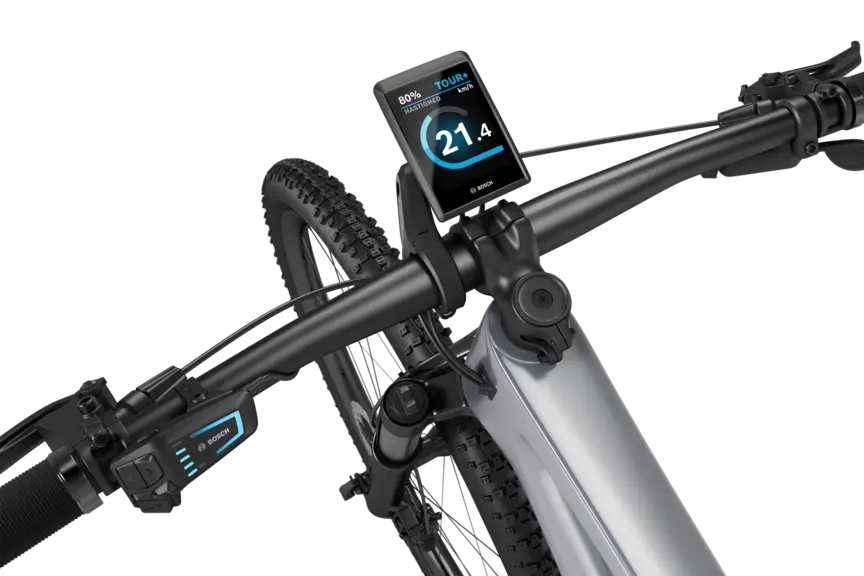 Et sølvfarvet eMountainbike med sort styr isoleret mod en hvid baggrund. På styret er der monteret en Kiox 500. Displayet viser hastigheden i km/t, batteristatus og køretilstand.