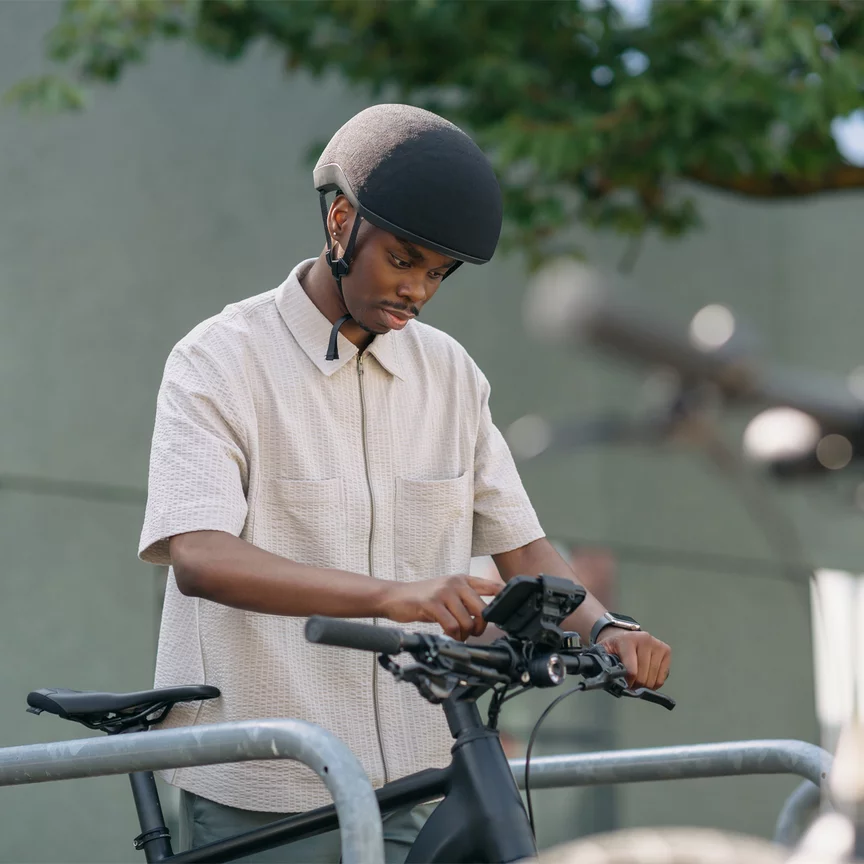A man stands at a bicycle rack, gripping the handlebars of his eBike and tapping on the smartphone mounted in the smartphone grip holder on the eBike.
