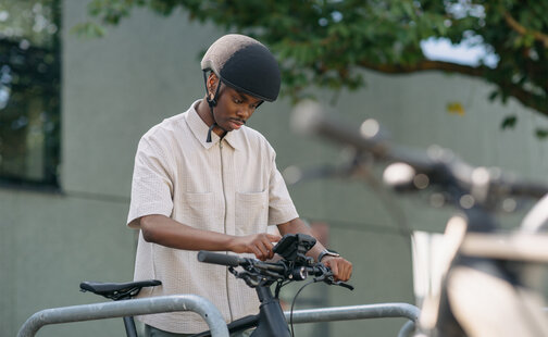 Ein Mann steht an einem Fahrradständer, hält den Lenker seines eBikes fest und tippt auf dem in der Smartphone-Grip-Halterung am eBike befestigten Smartphone.