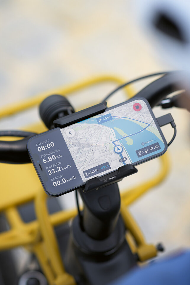 The smartphone is attached to a mount on the bicycle handlebars and is used as an eBike display for navigation, displaying route information and navigation instructions.