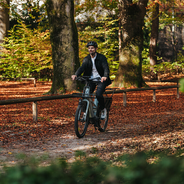 Ein Mann fährt lächelnd auf seinem eCargo Bike durch einen herbstlichen Park.