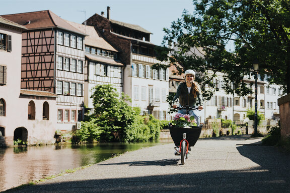 Eine Frau fährt lächelnd mit ihrem eCargo-Bike an einem Fluss entlang.