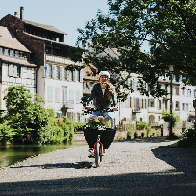 Une femme souriante roule sur son VAE Cargo le long d’un fleuve.