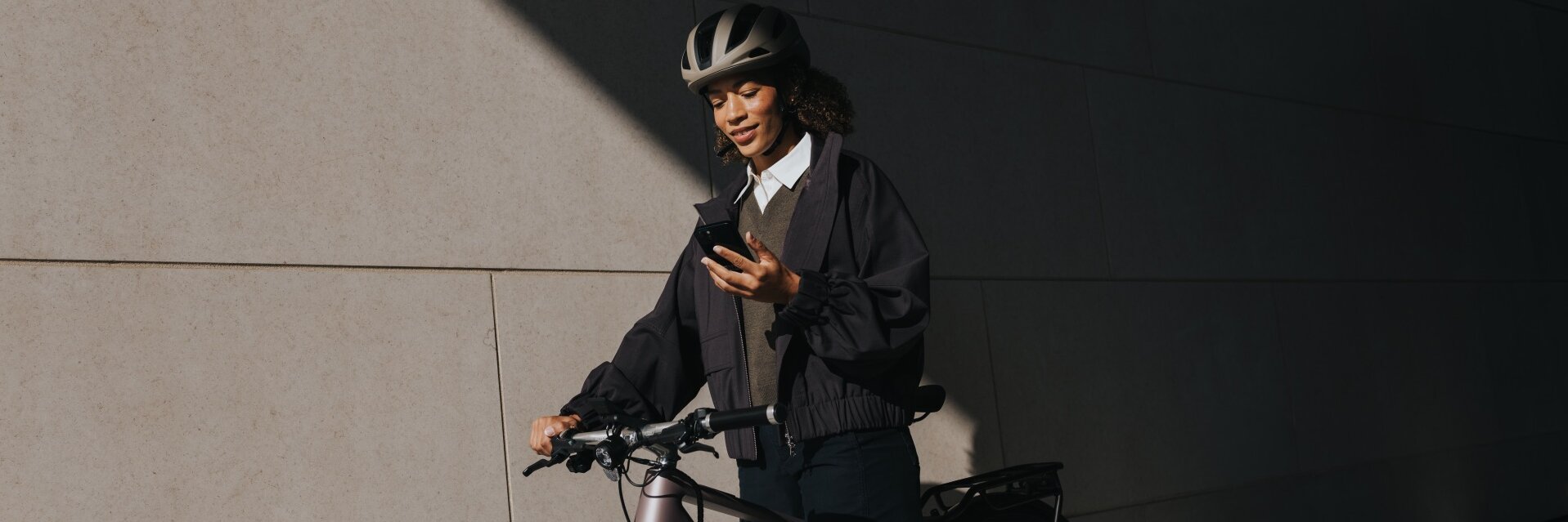 Eine Frau mit Helm steht mit ihrem eBike vor einem Gebäude und schaut auf ihr Smartphone.