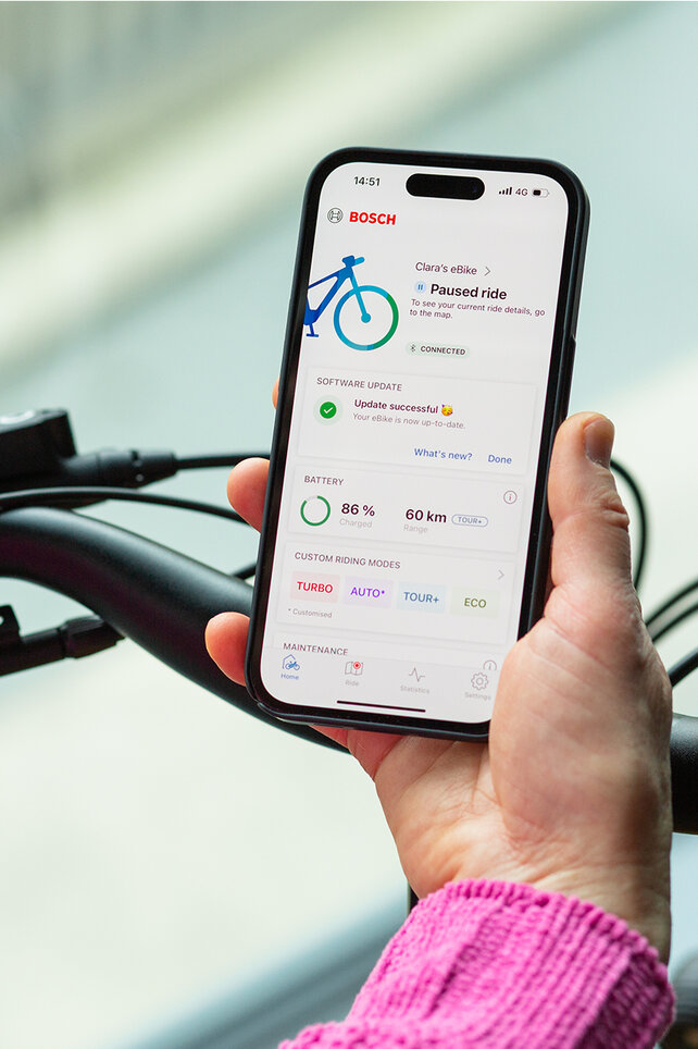 Blick über die Schulter einer Person, die ein Smartphone in der Hand hält, auf dem die eBike Flow App geöffnet ist.