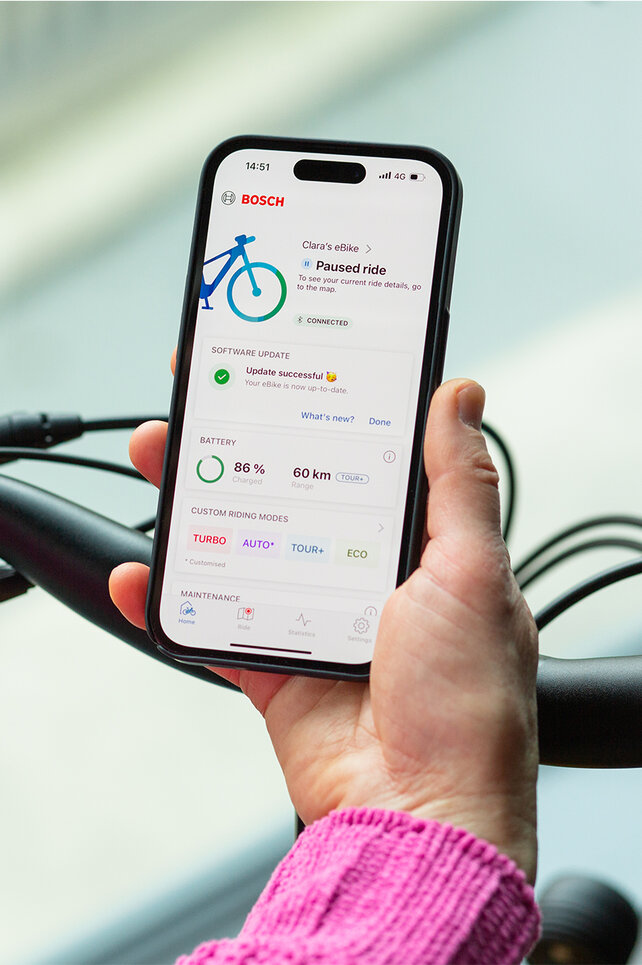 Blikk over skulderen til en person som holder en smarttelefon med eBike Flow-app åpen.