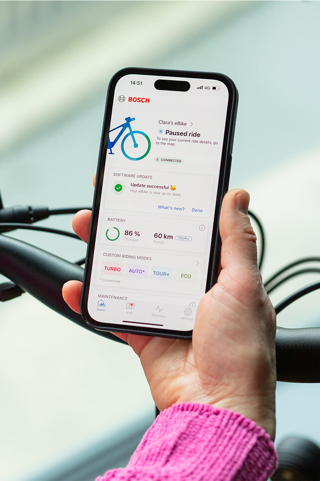Blick über die Schulter einer Person, die ein Smartphone in der Hand hält, auf dem die eBike Flow App geöffnet ist.