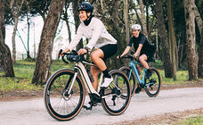 Two eBike riders riding on a road, with trees in the background.
