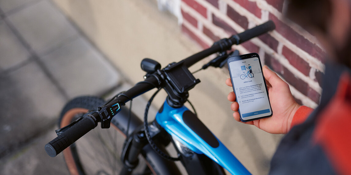 Una persona si siede sul suo eBike con il telefono in mano e sblocca l'eBike con eBike Lock.