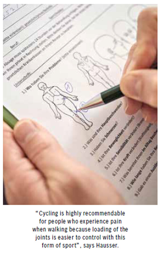 Close-up of a sheet of paper showing a drawn person. Someone marks the hip and knee with a ballpoint pen. Below the image, it says: 'Cycling is highly recommendable for people who experience pain when walking because loading the joints is easier to control with this form of sport, says Hausser.'