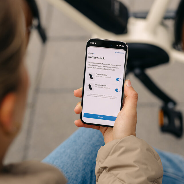 Blick über die Schulter einer jungen Frau, die auf ihrem Smartphone die Funktion Battery Lock über die eBike Flow App einstellt.