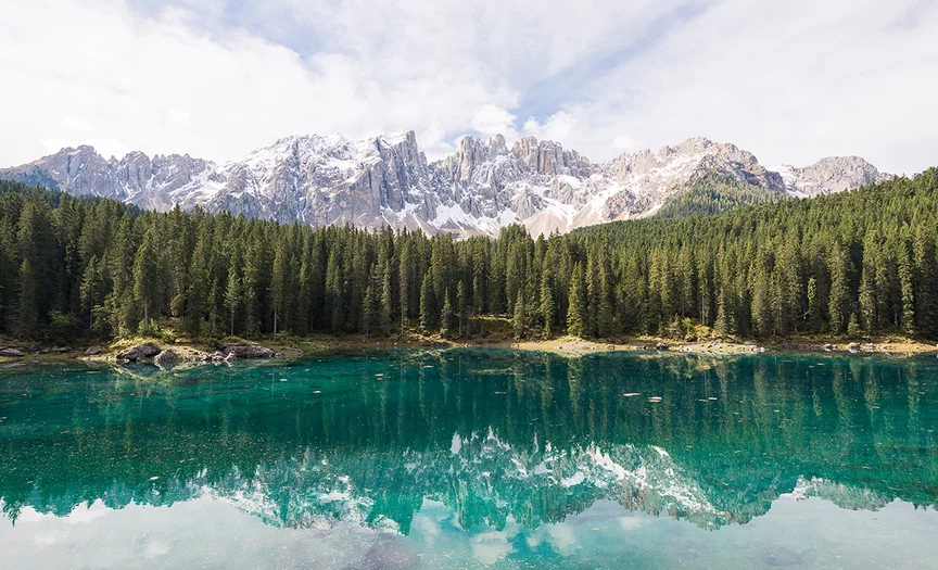 A turquoise mountain lake reflects the surrounding forest and mountain landscape.