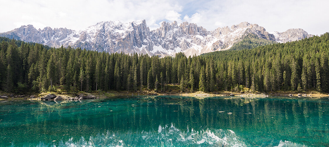 A turquoise mountain lake reflects the surrounding forest and mountain landscape.