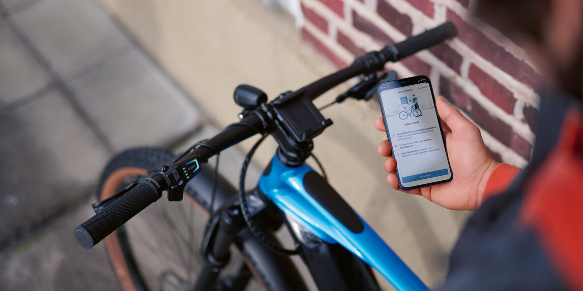 Eine Person sitzt auf ihrem eBike mit ihrem Smartphone in der Hand und entsperrt das eBike mit eBike Lock.