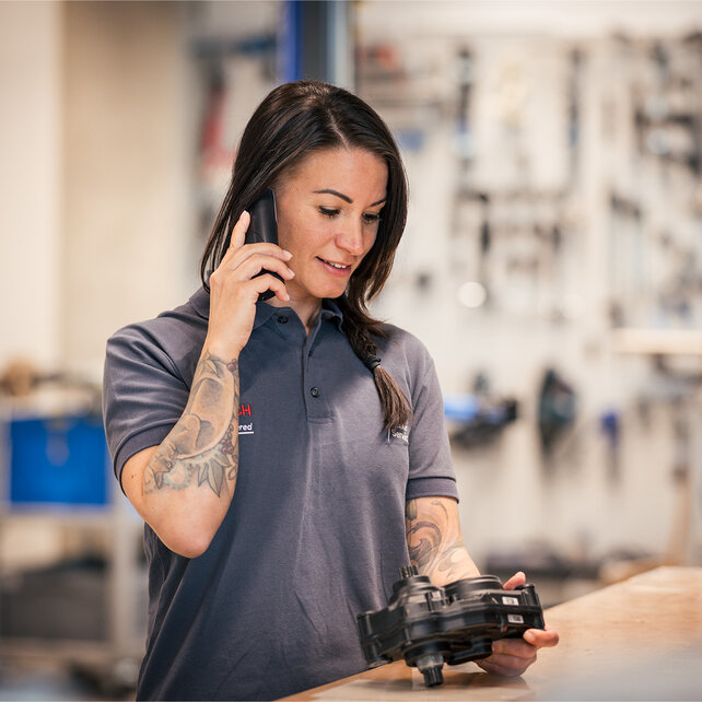 Une femme dans un atelier de réparation de vélos, tenant une VAE motorisation dans la main et parlant au téléphone.