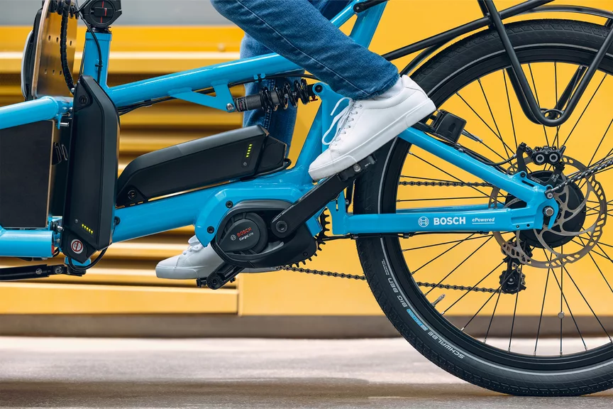 Nahaufnahme des mittleren Teils eines blauen eBike-Rahmens. Jemand tritt in die Pedale, und es sind zwei Akkus in Gebrauch zu sehen.