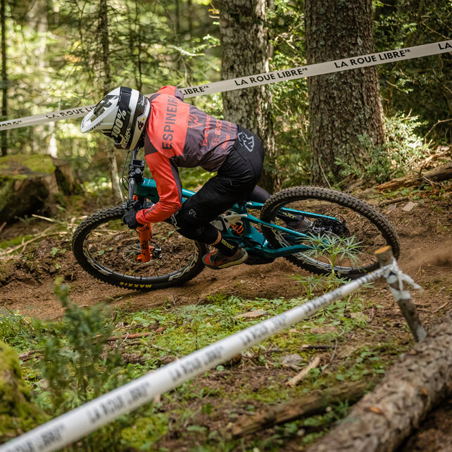 Il conducente di eMountain bike scende lungo un pendio nel bosco, segnato da nastri di delimitazione.