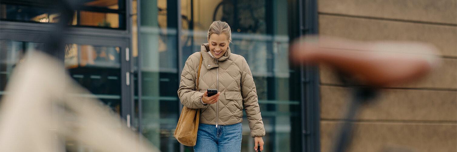 Lächelnde Frau hält Handy in der Hand und läuft auf ihr eBike zu.